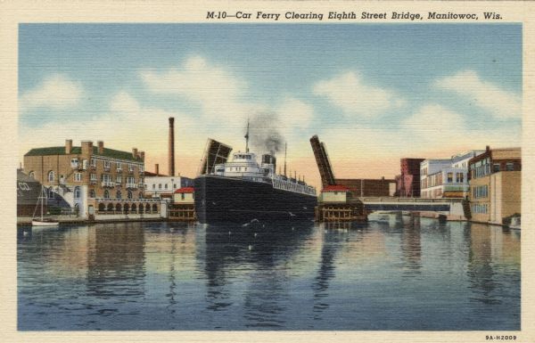 View across water towards a Lake Michigan car ferry going through a drawbridge. Caption reads: "Car Ferry Clearing Eighth Street Bridge, Manitowoc, Wis."