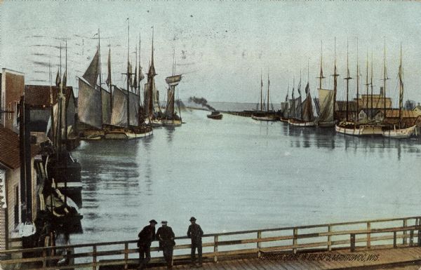 Scene of sailing vessels in the harbor near the mouth of the river. Three men are standing in silhouette on a bridge in the foreground.
