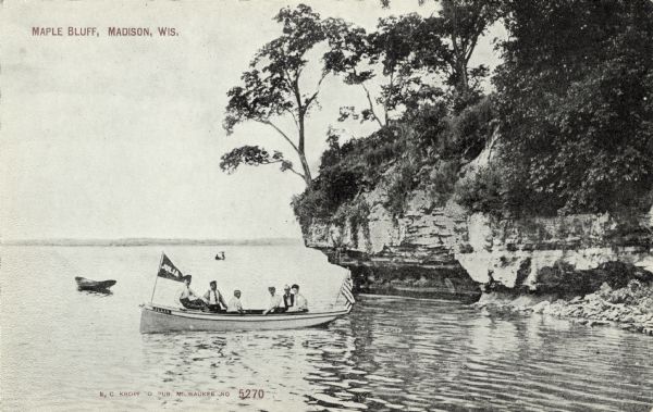 View across water towards a small boat named "Julia" at Maple Bluff (Lake Mendota) with six people in it. Caption reads: "Maple Bluff, Madison, Wis."