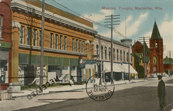 View looking across to the left at a city block of storefronts, and a church in the distance. A man is standing in the street in the right foreground. Caption reads: "Masonic Temple, Marinette, Wis."