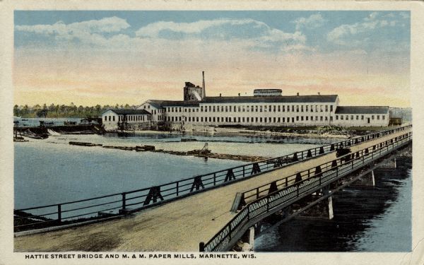 View of a road bridge crossing the Menominee River. There is a paper mill on the opposite shoreline. Caption reads: "Hattie Street Bridge and M. & M. Paper Mills, Marinette, Wis."