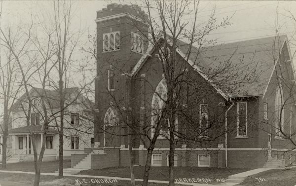 Sepia-toned postcard of a brick church with stained-glass windows. Caption reads: "M.E. Church, Markesan, Wis."