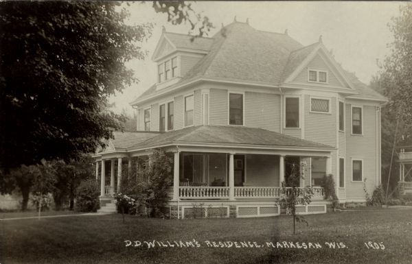 View across lawn towards a two-story home with an attic and a wrap-around porch with columns. Caption reads: "D.D. Williams Residence, Markesan, Wis."