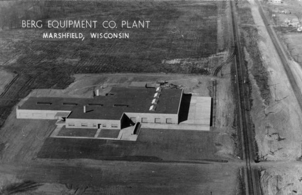 Aerial view of a factory near Marshfield. Railroad tracks are on the right. Caption reads: "Berg Equipment Co. Plant, Marshfield, Wisonsin."