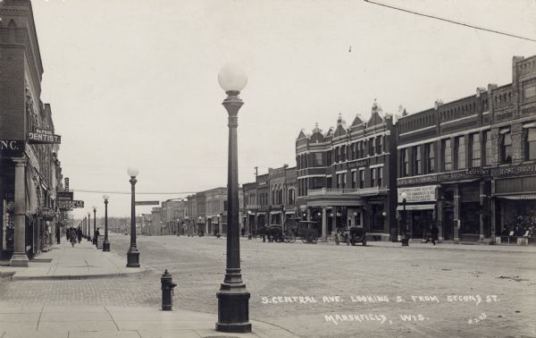 View of a paved street in a central business district lined with street lamps. Hotel Blodgett is on the right, and a fire hydrant is on the corner. Caption reads: "S. Central Ave. Looking S. from 2nd St. Marshfield, Wis."
