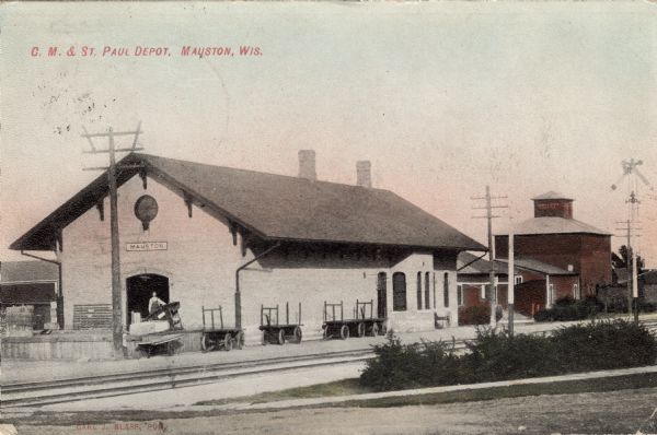 View of the C.M. & St. Paul depot with railroad tracks running along side. A man is standing in an arched service entrance.