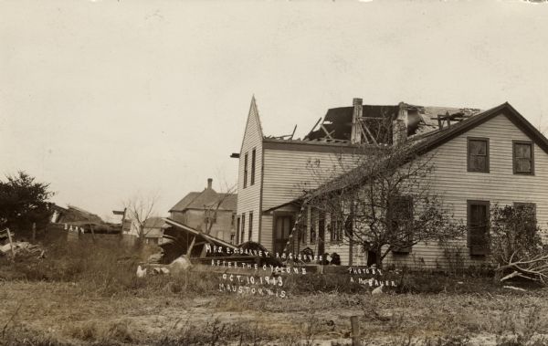 View towards a tornado-damaged home with most of the roof missing and a collapsed barn. A chicken is in the yard. Captions read: "Barn" and "Mrs. E.C. Barney Residence After the Cyclone, Oct 10, 1913, Mauston, Wis."