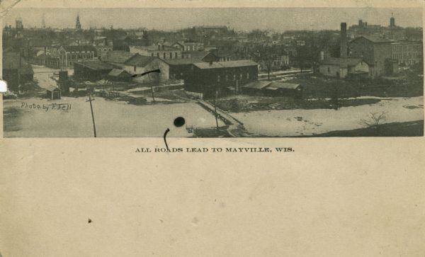 Aerial panoramic view of central Mayville over a frozen river. Caption reads: "All Roads Lead to Mayville, Wis."