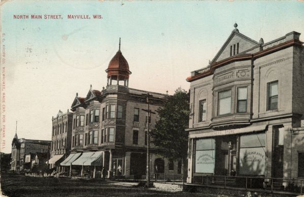View from street towards three blocks of Main Street. A general store is on the far right, and the building on the corner in the center has an ornate roof tower. Caption reads: "North Main Street, Mayville, Wis."