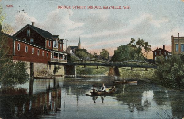 View of the bridge crossing the Rock River at Bridge Street. People are in rowboats on the river. Caption reads: "Bridge Street Bridge, Mayville, Wis."