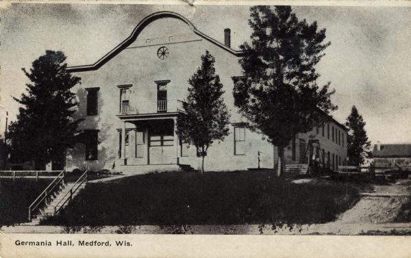 Exterior view of Germania Hall, a saloon and meeting place. There is a square balcony over the entrance. Caption reads: "Germania Hall, Medford, Wis."