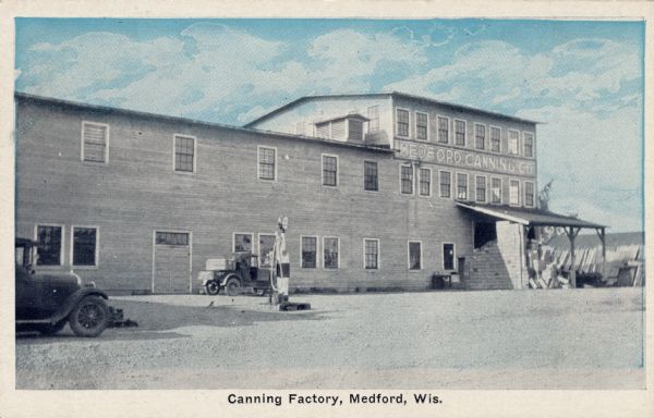 Exterior view of the canning factory. Two trucks are parked in front near a pump. Caption reads: "Canning Factory, Medford, Wis."