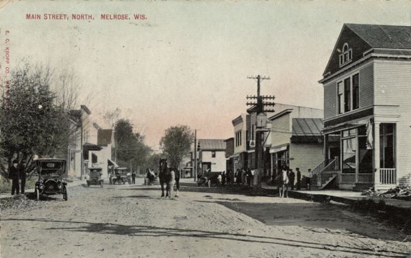 View of Main Street with cars and horses. Caption reads: "Main Street, North, Melrose, Wis."
