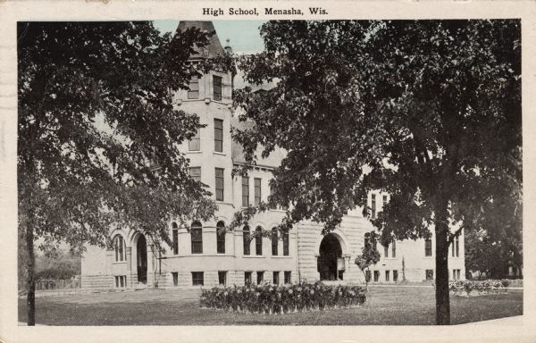 Exterior view of a high school, with flower beds in the front lawn. Caption reads: "High School, Menasha, Wis."