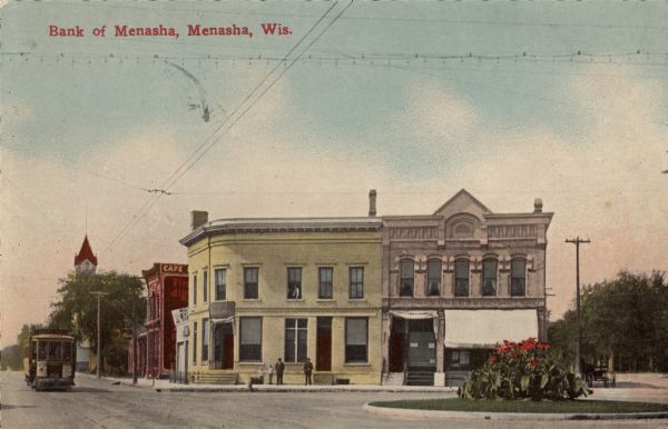 View from street towards a corner bank and surrounding buildings. A streetcar is coming up the street. Caption reads: "Bank of Menasha, Menasha, Wis."