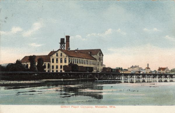 View of a paper mill on the banks of the Fox River. Menasha in the distance. Caption reads: "Gilbert Paper Company, Menasha, Wis."