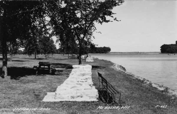 View of a park on the banks of the Fox River, with picnic tables and stone grills near trees. Caption reads: "Jefferson Park, Menasha, Wis."