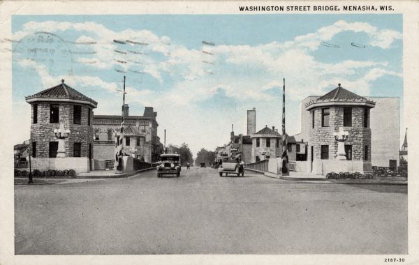 View of a drawbridge in a business district. Stone structures are at each corner. Automobiles are in the street. Caption reads: "Washington Street Bridge, Menasha, Wis."