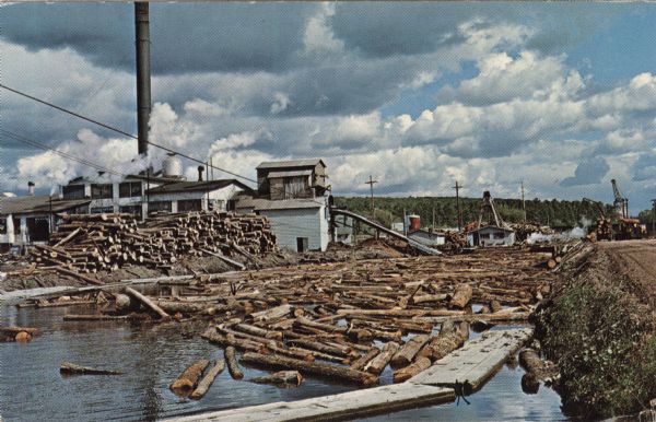View of a log jam on the Wolf River next to a saw mill. Caption on back reads: "first built in 1908 . . . 20,000,000 feet lumber cut a year . . . largest in Midwest . . . only industry in Menominee County . . . on Wolf River."