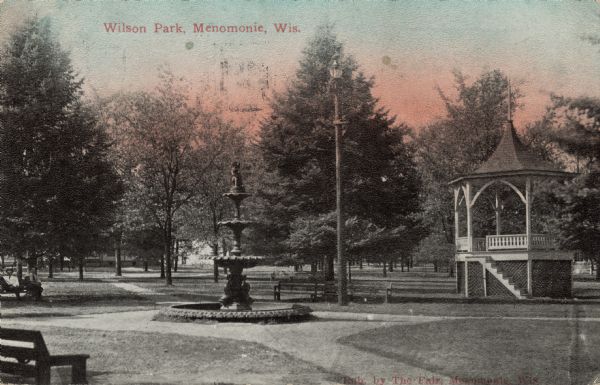 View of the gazebo and fountain at Wilson Park. Two men are sitting on a bench on the far left. Caption reads: "Wilson Park, Menomonie, Wis."