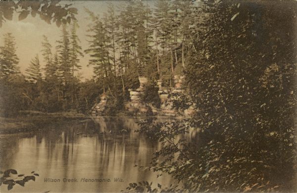 View of Wilson Creek surrounded by pines and sandstone cliffs. Caption reads: "Wilson Creek, Menomonie, Wis."