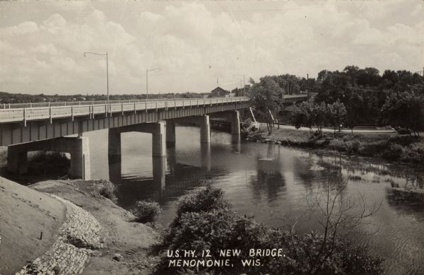 View of a highway bridge spanning the Red Cedar River, and a road along the far shoreline. Caption reads: "U.S. Hy 12 New Bridge, Menomonie, Wis."
