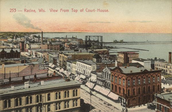 Text at top reads: "Racine, Wis. View from Top of Court-House." An elevated view of Racine including the harbor. Buildings, rooftops, signs, the gas works storage tank, Lake Michigan, harbor facilities and the breakwater can be seen.
