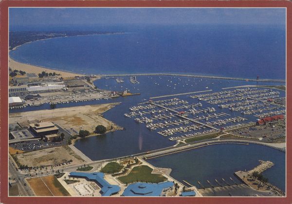 Text on reverse: "Magnificent view of Lake Michigan shoreline from Racine Harbor to Wind Point Lighthouse. Photo Courtesy RAMAC." Aerial view of Racine Harbor and North Bay. Boats are docked inside the breakwater.