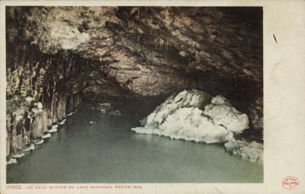 Text on front reads: "Ice Cave. Winter on Lake Michigan. Racine, Wis." The logo for the Detroit Publishing Company is in the lower right corner. Water level view of an ice cave on the rocky shore. Snow has accumulated at the water line and icicles are hanging from the ceiling.