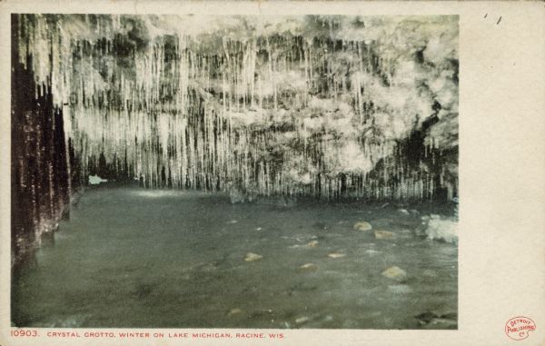 Text on front reads: "Crystal Grotto. Winter on Lake Michigan. Racine, Wis." Water level view of an ice cave on the rocky shore. So many icicles are hanging from the ceiling that it looks like a crystal curtain.