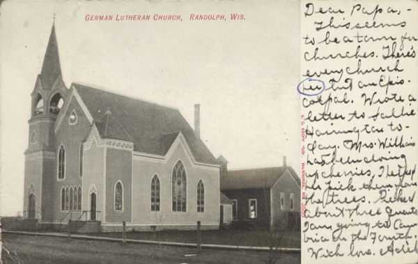 Text on front reads: "German Lutheran Church, Randolph, Wis." View of a church, with a smaller building behind it. The church faces an unpaved road lined with posts.