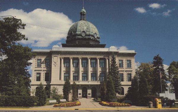 Text on reverse: "Oneida County Courthouse located at Rhinelander, Wisconsin." The Courthouse is built of stone and has a copper dome. The front has many windows and columns. Surrounded by trees with gardens and benches at the entrance.