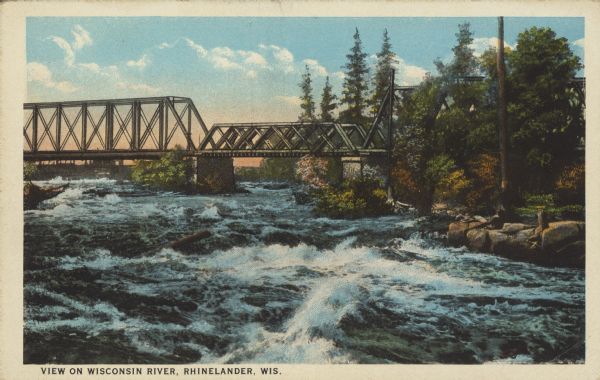 Text on front reads: "View on Wisconsin River, Rhinelander, Wis." A trestle railroad bridge crosses turbulent water on the Wisconsin River. The rocky shoreline and trees are on the right.