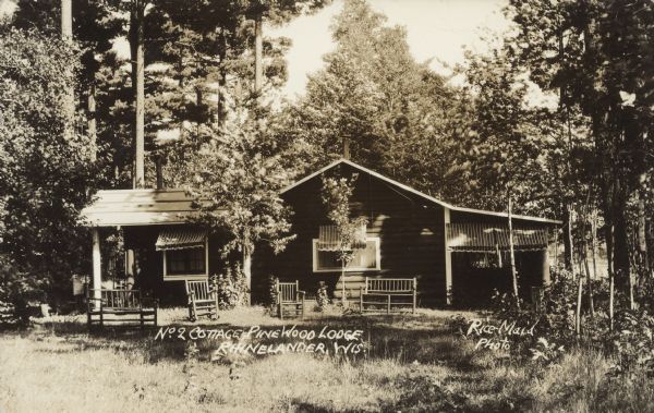 Text on front reads: "No. 2 Cottage, Pinewood Lodge, Rhinelander, Wis." A large log cabin is surrounded by trees. Many windows have awnings. Rustic wood seating is arranged in the yard.