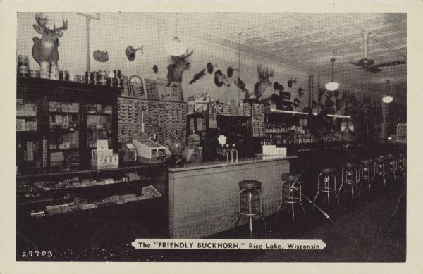 Text on front reads: "The 'Friendly Buckhorn,' Rice Lake, Wisconsin." Text on reverse reads: "No vacation trip to Northern Wisconsin is complete without a visit to the 'FRIENDLY BUCKHORN' at Rice Lake, Wisconsin. Hundreds of curios on display including the 'WORLD'S RECORD DEER.' "The Buckhorn Tavern had an amazing display of taxidermy and curios including some hoaxes, a shovel-tailed snowsnake, a dingbat and a fur herring. A large selection of tobacco pipes are displayed on the wall behind the counter. Originally the Buckhorn was a billiard parlor.