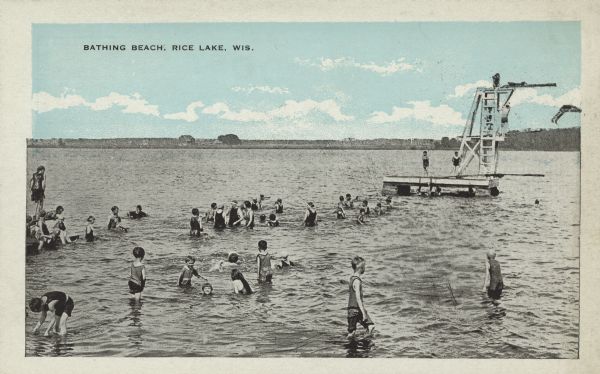 Text on front reads: "Bathing Beach, Rice Lake, Wis." Many adults and children are swimming and diving at the beach. There is a pier on the left and an elaborate diving board and platform on the right. The opposite shore can be seen on the horizon.