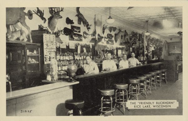 Text on front reads: "The 'Friendly Buckhorn,' Rice Lake, Wisconsin." Text on the reverse reads: "No vacation trip to Northern Wisconsin is complete without a visit to the 'FRIENDLY BUCKHORN' at Rice Lake, Wisconsin. Hundreds of curios are on display including the 'WORLD'S RECORD DEER.'" Four Bartenders are standing behind counter. The Buckhorn Tavern had an amazing display of taxidermy and curios including some hoaxes, a shovel-tailed snowsnake, a dingbat and a fur herring. Originally the Buckhorn was a billiard parlor.