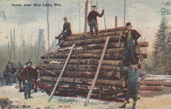 Text on front reads: "Scene Near Rice Lake, Wis." Five lumberjacks pose with a load of logs on a sled pulled by horses. Two skids lean against the logs. The lumberjacks are holding the tools used to load the sled.
