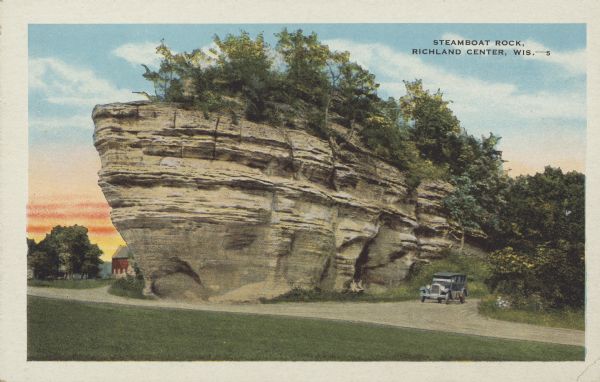 Text on front reads: "Steamboat Rock, Richland Center, Wis." A large formation, crowned with trees, juts over a dirt road. An automobile is on the road on the right. A farm can just be seen behind the formation on the left. More trees are in the background.