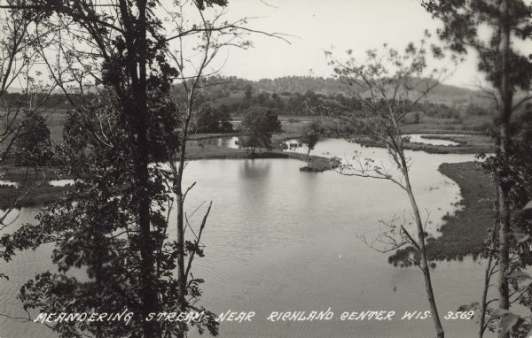 Text on front reads: "Meandering Stream Near Richland Center, Wis." Elevated view of a stream, probably the Pine River or a tributary, winding through a valley. Many trees and hills are in the distance.
