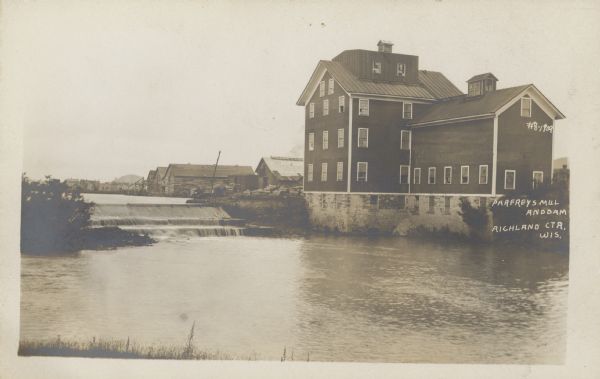 Text on front reads: "Parfrey's Mill and Dam. Richland Ctr. Wis." A grist mill, dam and millpond on the Pine River. More buildings are behind the mill. The mill was built in 1872 by Ira Haseltine, the founder of Richland Center, then sold to A.C. Parfrey. It was torn down in 1934. The dam was removed in the 1990s.