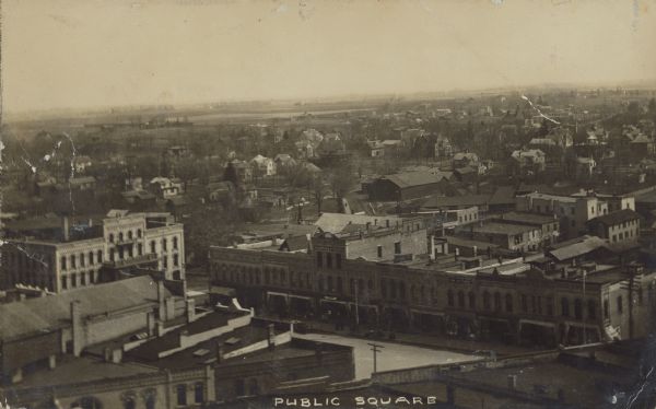 Text on front reads: "Public Square." View from a tall building over the Public Square with buildings and dwellings of the town spreading out to the horizon.
