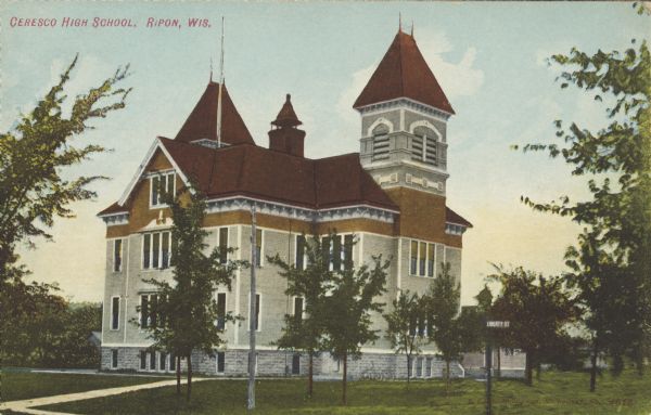 Text on front reads: "Ceresco High School, Ripon, Wis." A two-story  schoolhouse with basement windows along the foundation, and attic space. The school has two towers, a chimney, sidewalks and trees.