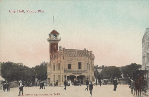 Text on front reads: "City Hall, Ripon, Wis." View across public square towards a brick building with ornate exterior decorations and a bell tower with a balcony. There are many pedestrians moving across the square, and a horse-drawn buggy on the right is in front of a building. Trees are in the background. The Ripon City Hall building was built in 1900 and removed in 1967. It also housed the post office and fire department.