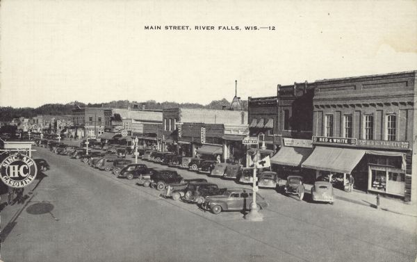 Text on front reads: "Main Street, River Falls, Wis." Main street with a parking boulevard in the center, filled with automobiles. Several people are out and about. Businesses can be seen on both sides, many with awnings and signs. On the right is "H-C Sinclair Gasoline", on the left is "Red & White".