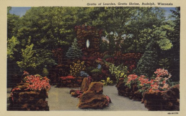 Text on front reads: "Grotto of Lourdes, Grotto Shrine, Rudolph, Wisconsin." A garden with flowers, rocks, shrubs and paths. A rock shrine with a statue of the Virgin Mary in a niche. In the background are trees.