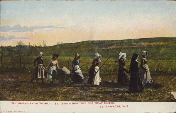 Text on front reads: "'Returning from Work.' St. John's Institute for Deaf Mutes. St. Francis, Wis." A group of six women holding implements and a nun are walking in a field. One of the woman is pushing a wheelbarrow. In the background is a road and a hill with a horse-drawn wagon. The school was operated from 1876 until 1976.