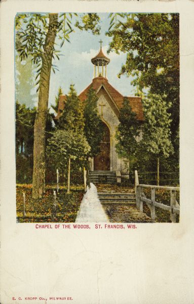 Text on front reads: "Chapel of the Woods, St. Francis, Wis." A stone chapel surrounded by trees with a belfry. There is a walkway with two sets of stairs and a handrail on one side leading up to the entrance.