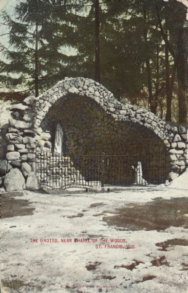Text on front reads: "The Grotto, near Chapel of the Woods, St. Francis, Wis." The Grotto of Our Lady of Lourdes was built in 1894 by German-born seminarian Paul Dobberstein. There is snow on the ground and mature pine trees fill the background. The Grotto fell into disrepair, was renovated, then rededicated in September of 2009.