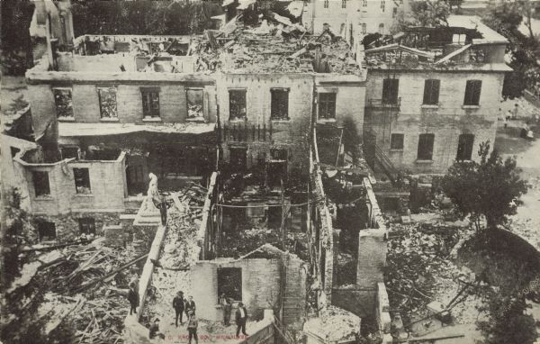 Text on reverse reads: "Bird's Eye View of Destruction, St. John's Institute for Deaf Mutes, St. Francis, Wis. Aug. 1, 1907." A partially burned stone and brick building with people surveying the damage. The fire began in the chapel roof, and no one was injured.